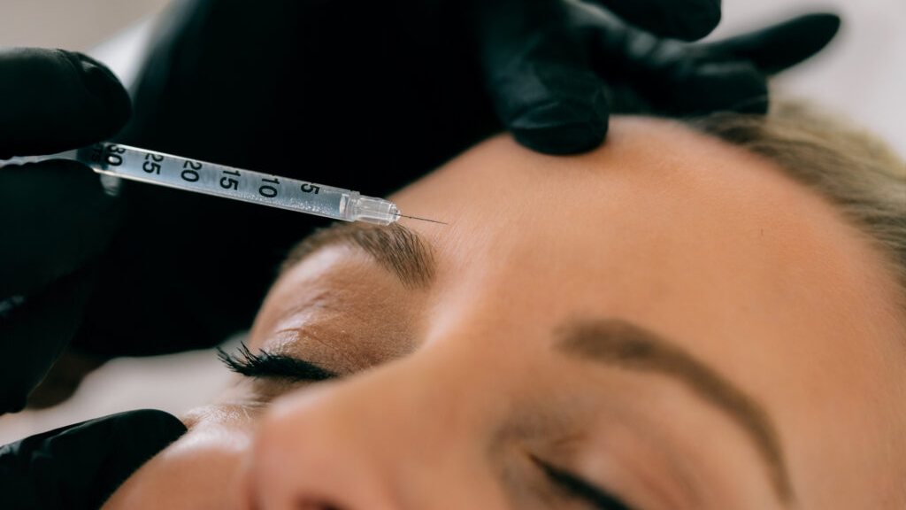 A gloved practitioner giving an injectable treatment to a client's forehead