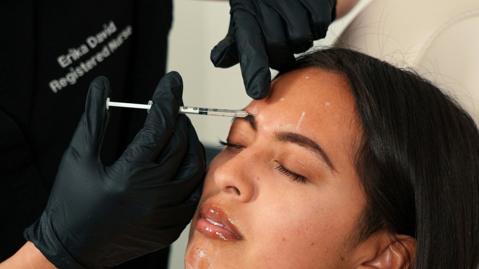 A practitioner in black gloves giving a client an injectable treatment