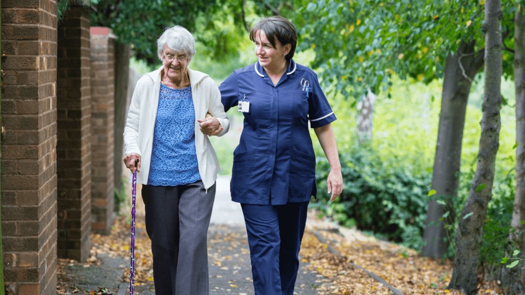 A home carer walking arm in arm with an older woman using a walking stick