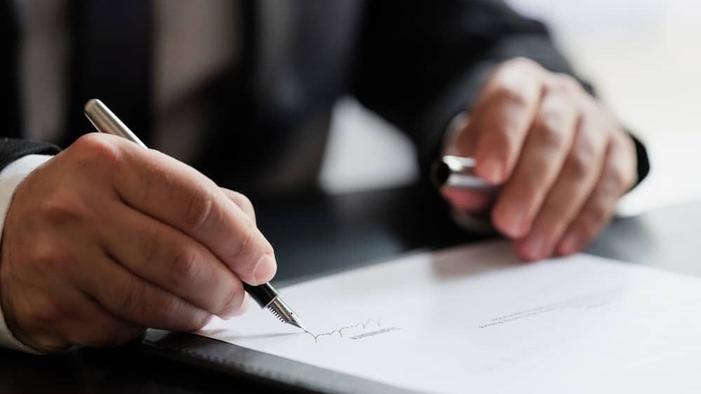 A person in a suit signing a document with a fountain pen
